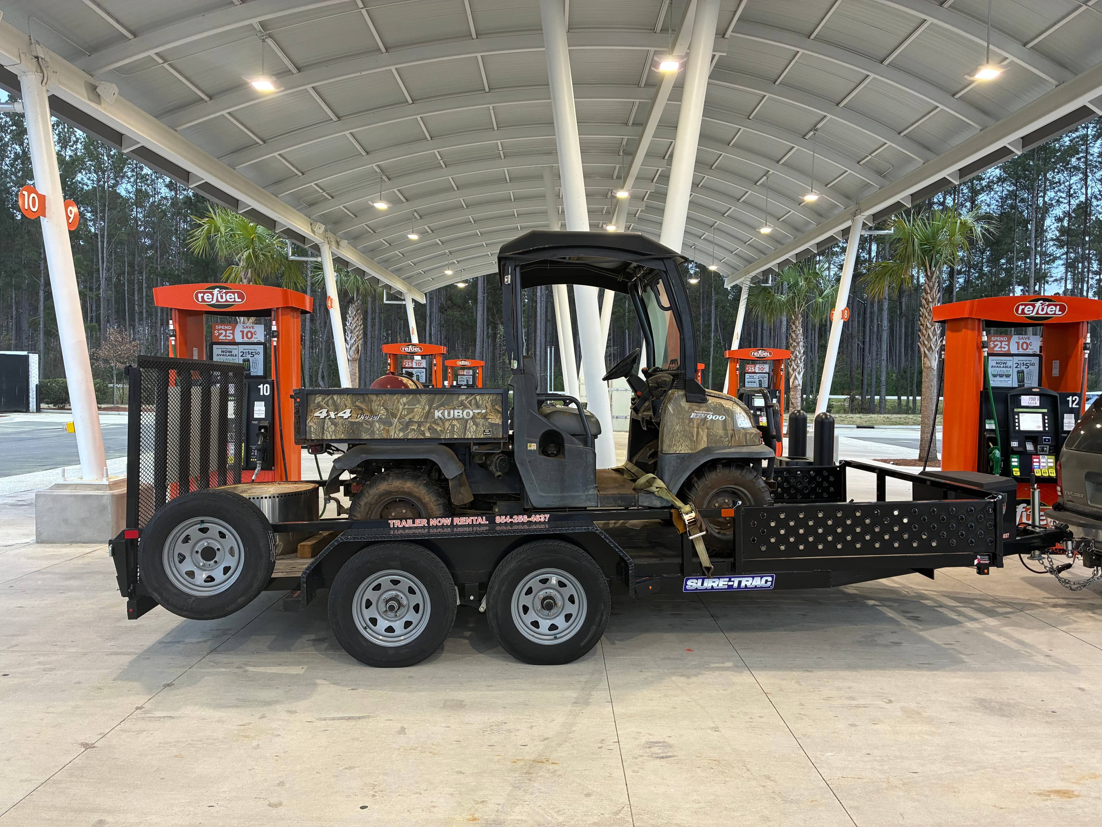 Black and white Kubo utility vehicle on utility trailer at refuel station