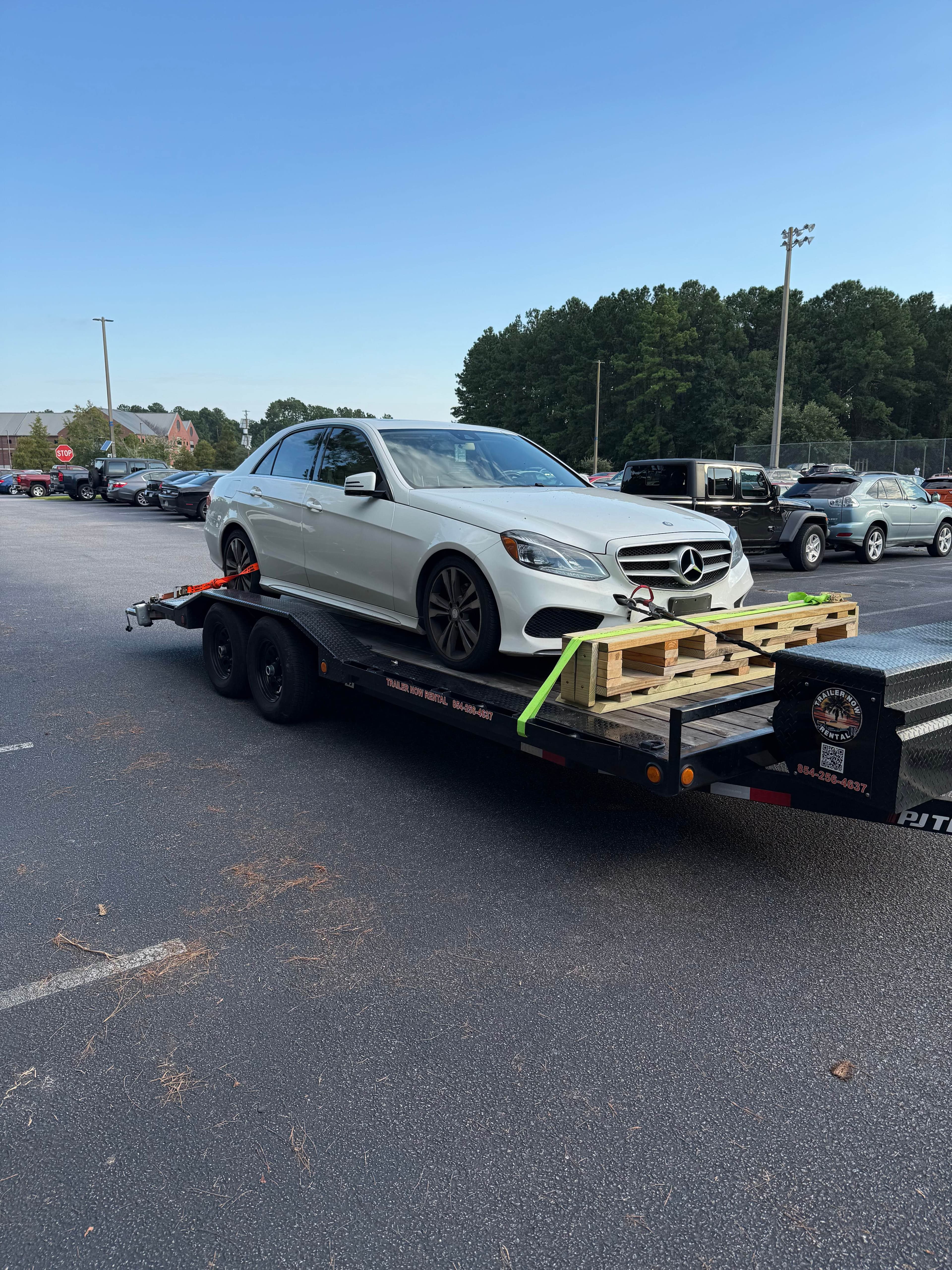 White Mercedes sedan on car hauler at car lot
