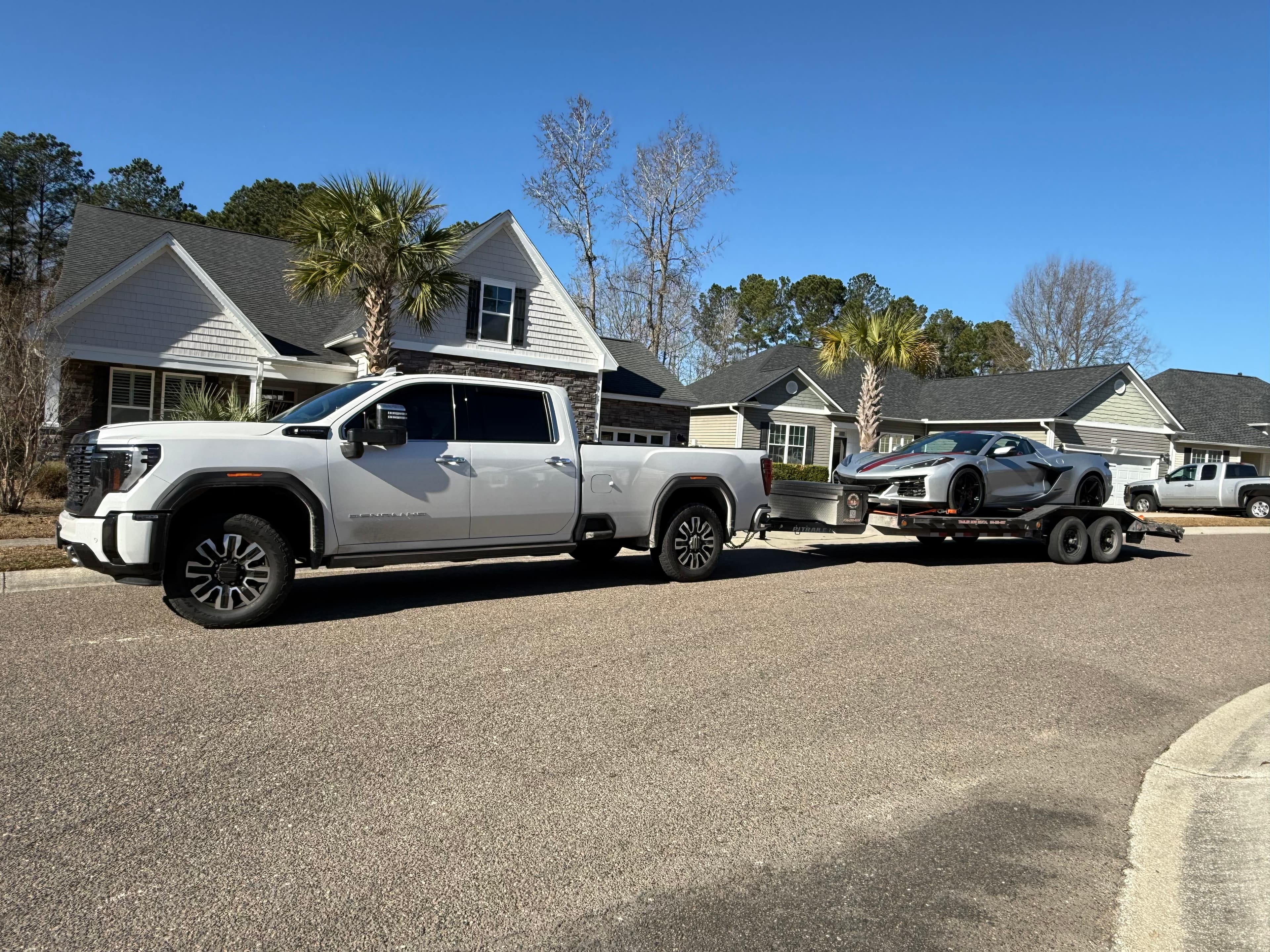 White GMC Sierra hauling gray sports car on car hauler