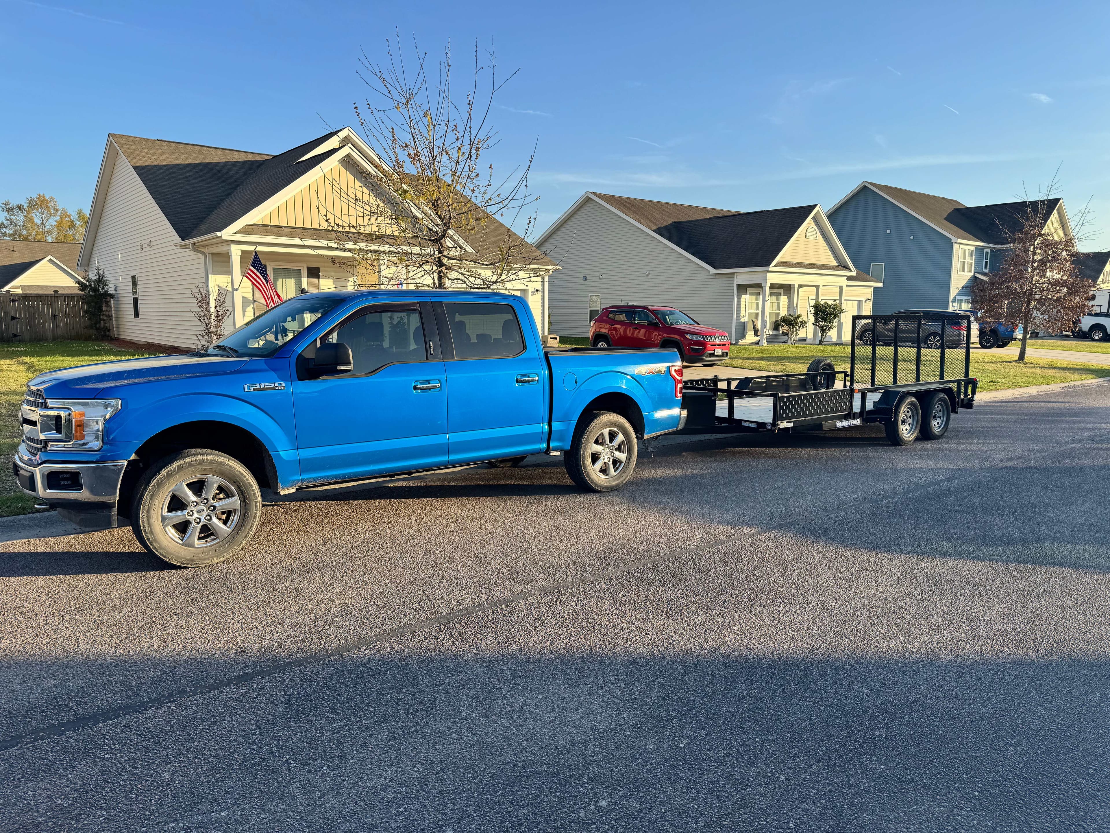 Bright blue Ford F-150 with utility trailer in residential area